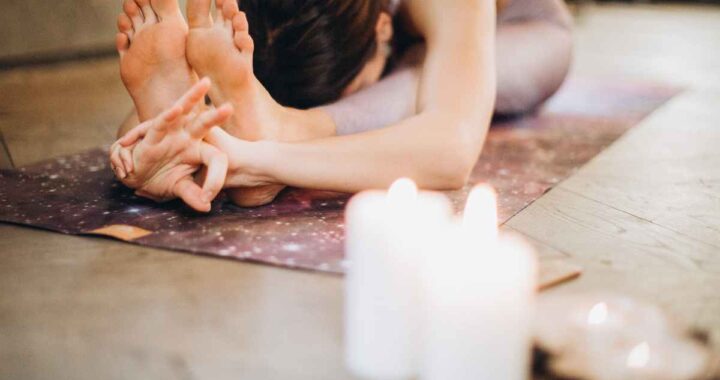 A person in a yoga pose in behind four lit candles, with their head resting on their knees.