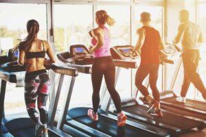 Four people, two women and two men, running on treadmills in a gym.
