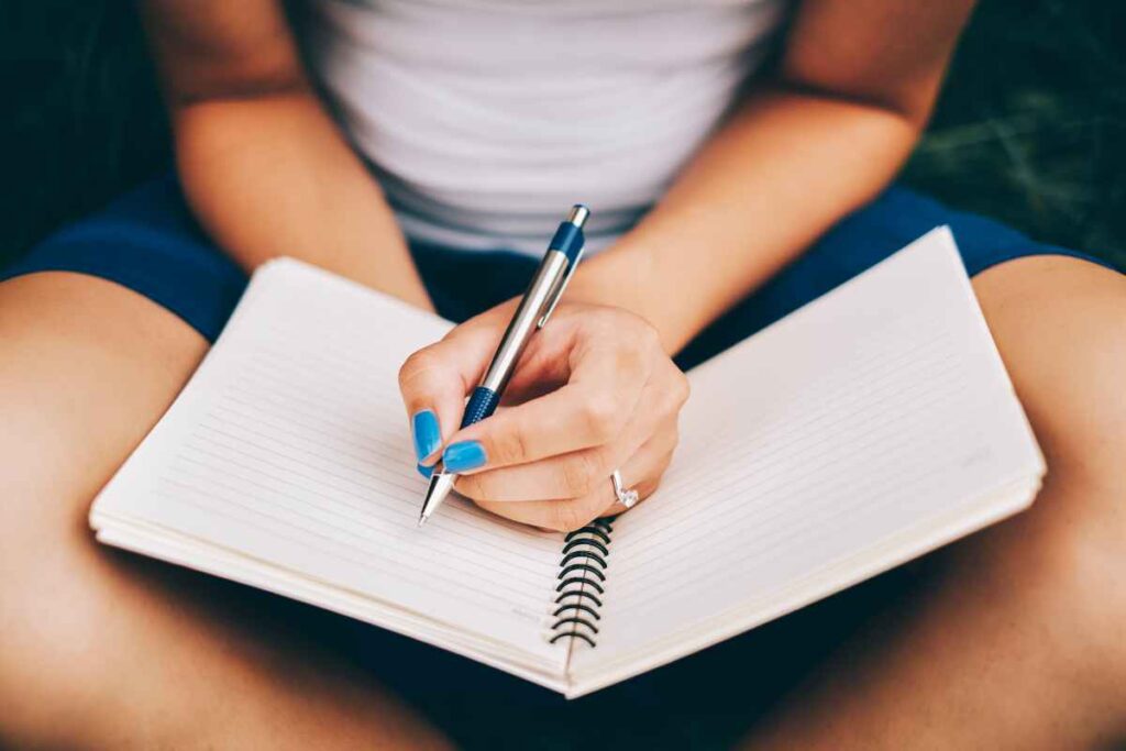 A woman holding a pen and a blank notebook preparing to start journaling for spiritual growth. This is intended to represent the 4th of 6 spiritual practices for improving your intuition