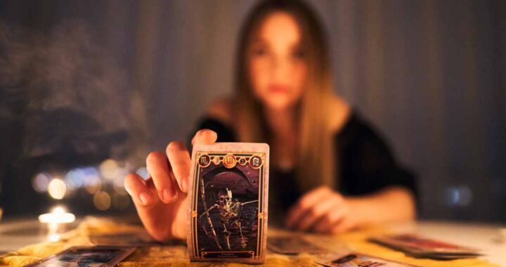 Woman with Death Tarot Card in Candlelit Darkness