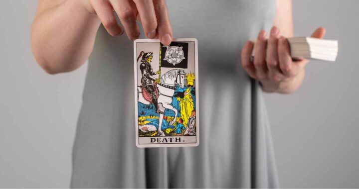A woman holds the Rider-Waite Death card, symbolizing transformation and renewal in tarot readings.