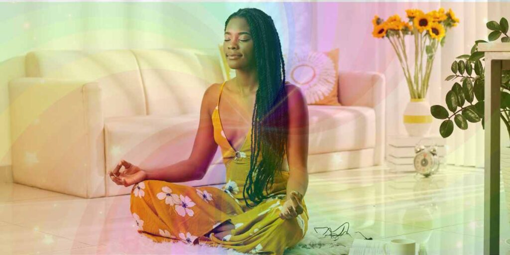 An African American woman sits cross-legged on the floor in her living room, eyes closed in meditation. Swirling transparent colors surround her, symbolizing visualization techniques. She appears happy and at peace. Demonstrates the 1st of 6 spiritual practices for improving your intuition.