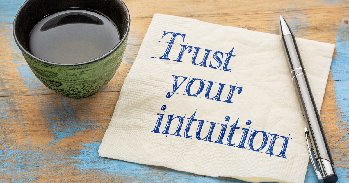 A cup of tea and a napkin with the words "trust your intuition" in blue on it. A pen is next to the napkin. This image is a message about the importance of developing intuition.