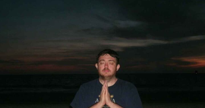 John Culbertson sits in meditation with eyes closed on a quiet beach at sunset, hands in prayer position. For the blog post what happens during a session with John Culbertson
